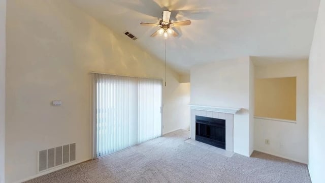 Living room with vaulted ceiling, fireplace, ceiling fan, and sliding glass door.