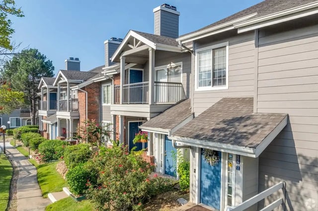 Row of townhouse-style apartment buildings with blue doors, balconies, and landscaped path.