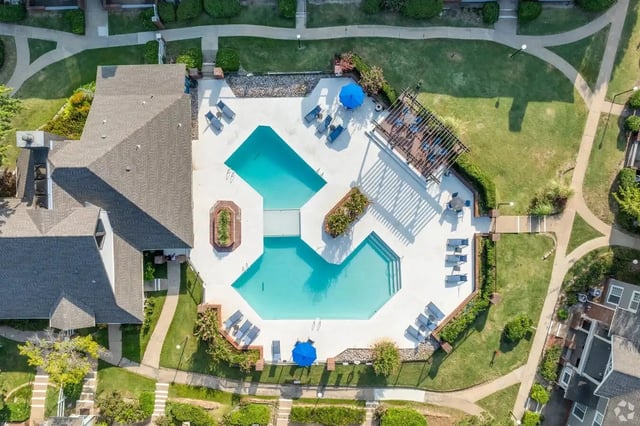 An aerial view of an apartment complex pool area with lounge chairs and umbrellas.