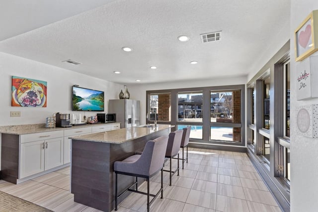 Modern communal kitchen with island, granite counters, bar seating, and pool-view windows.
