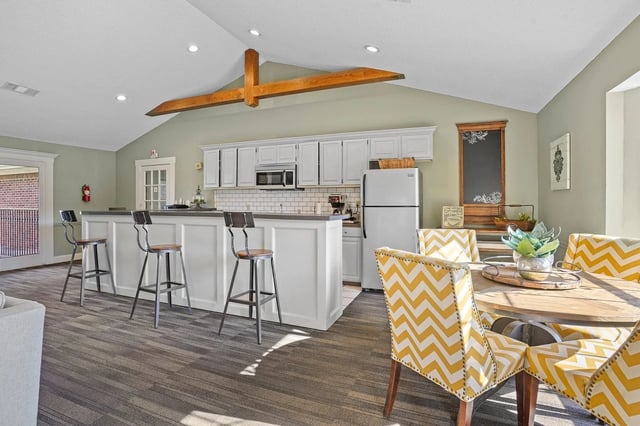 Open-concept kitchen with white cabinets, a breakfast bar with metal stools, and a round dining table with chevron chairs.