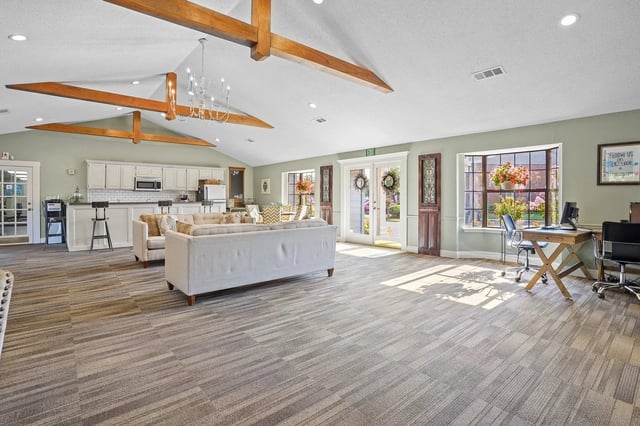 Bright communal lounge with sofas, a kitchen bar, and a work desk in a clubhouse.