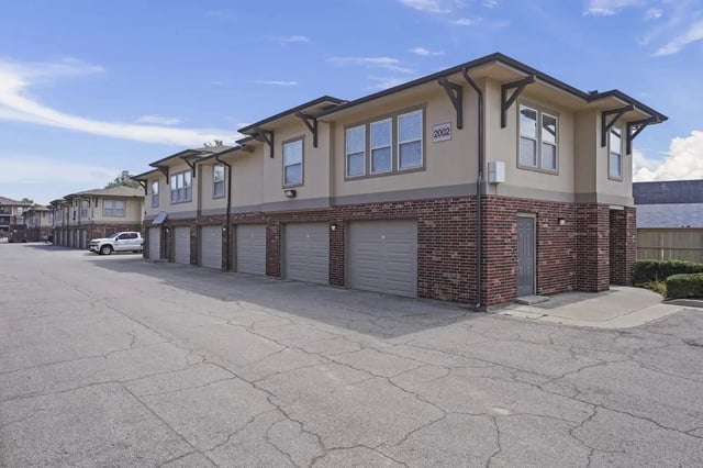 Row of two-story apartment buildings with attached garages along a paved lot.
