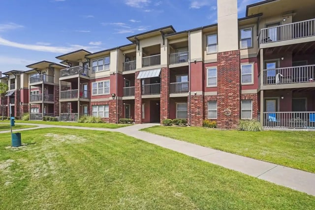 Exterior view of a multi-story apartment building with balconies and a green lawn.