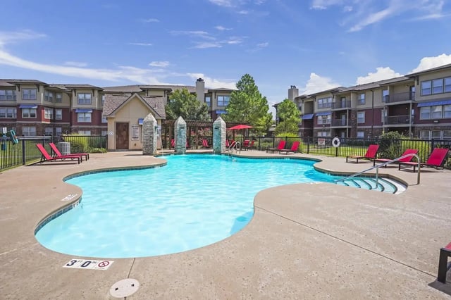 Outdoor pool at a multifamily community with red lounge chairs and surrounding buildings.