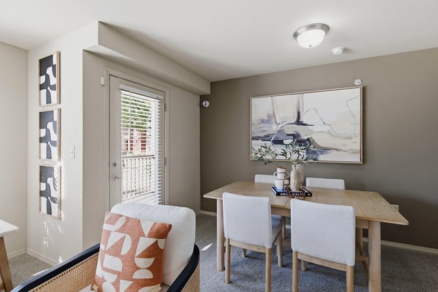 Living and dining area with a chair, dining table and chairs, and a door leading outside.