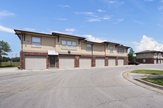 Exterior of apartment buildings with attached garages and a parking lot.