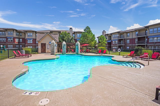 Resort-style swimming pool with lounge chairs and apartment buildings in the background.
