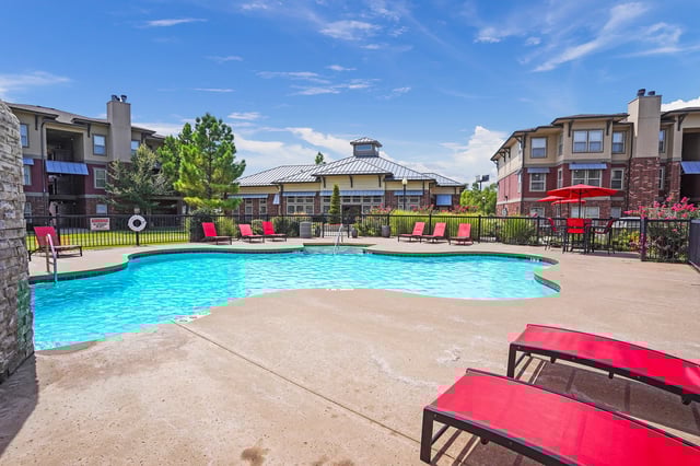 Outdoor swimming pool with lounge chairs and apartment buildings in the background.