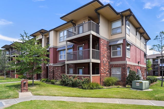 Exterior view of a multifamily apartment building with red brick accents and balconies.