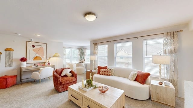 Modern living room with a white sectional sofa, orange accent chairs, a coffee table, and a desk area.