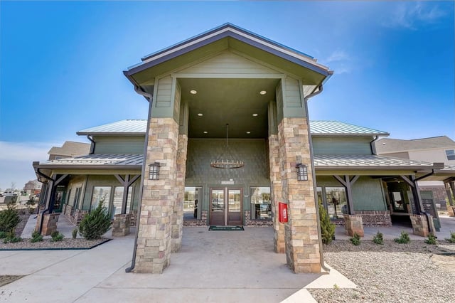 Modern apartment building entrance with stone pillars and green siding.