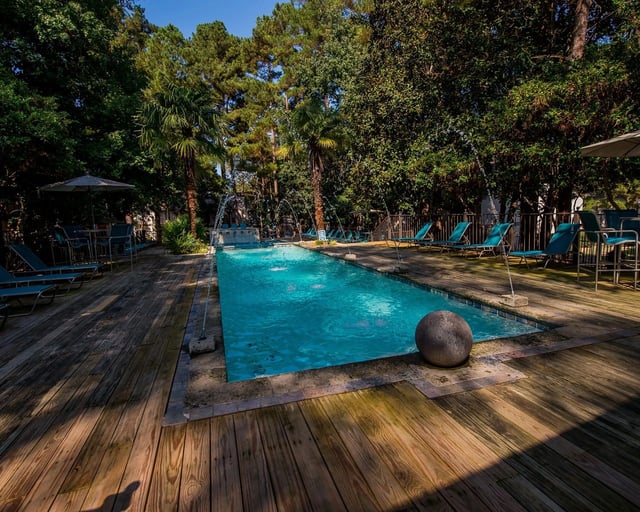 Outdoor pool with wooden deck, lounge chairs, and surrounding trees.