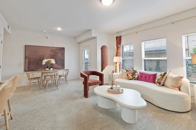 Living room and dining area with a white curved sofa, pink accent chair, and a round dining table.