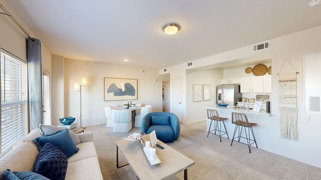 Modern living room and kitchen with white cabinets, stainless steel appliances, and bar seating.