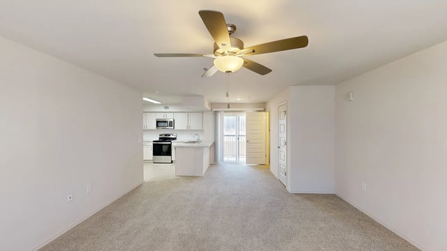 Living room and kitchen area of an apartment with a ceiling fan.