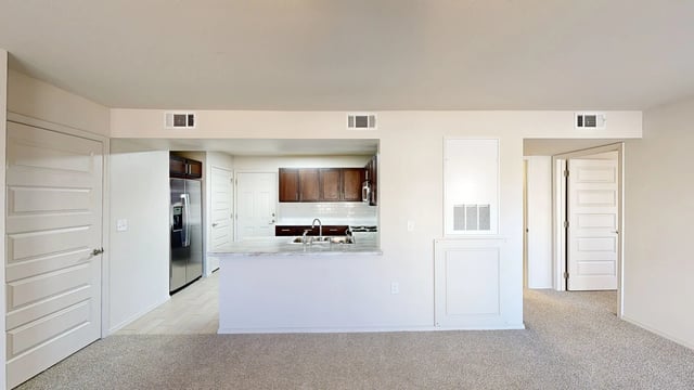 Open concept living area with a view into the kitchen, featuring dark wood cabinets, granite countertops, and stainless steel appliances.