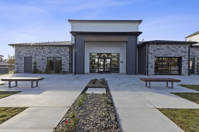 Exterior view of a modern apartment community entrance with glass doors and stone façade.