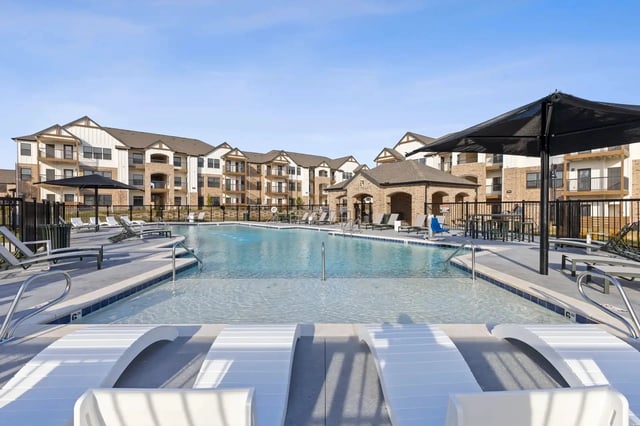 Outdoor pool at a multi-family apartment community with lounge chairs and umbrellas.