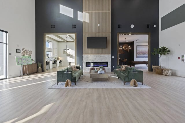 Spacious modern apartment lobby with two green sofas facing a stone fireplace and open entryways.