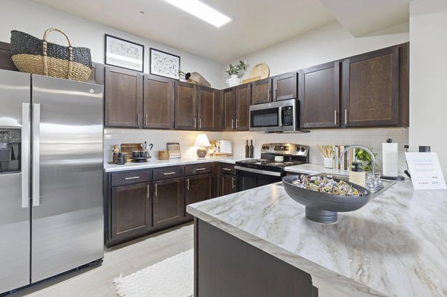 Modern kitchen with dark wood cabinets, stainless steel appliances, and a marble island.