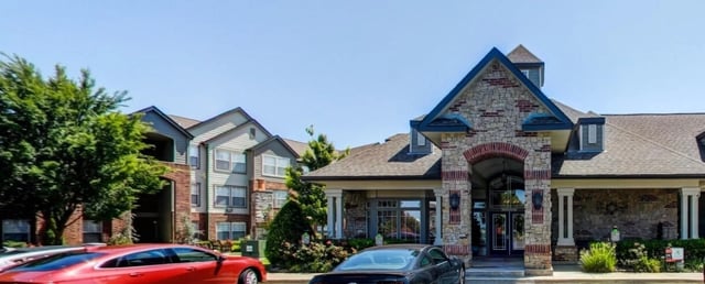 Exterior view of apartment buildings and a clubhouse with cars parked out front.