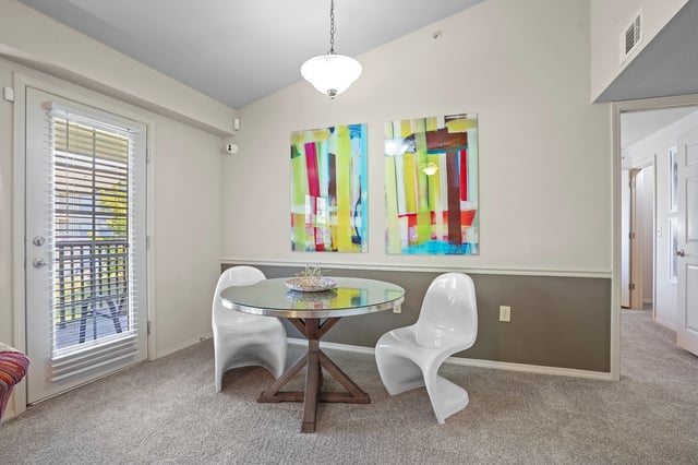 Dining area with a round glass-top table and two white chairs, next to a door with a balcony view.