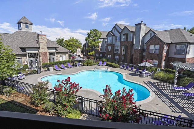 Outdoor pool in an apartment complex with purple lounge chairs and surrounding buildings.