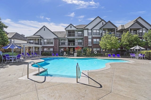 Outdoor apartment community pool with lounge chairs and umbrellas, with residential buildings in the background.