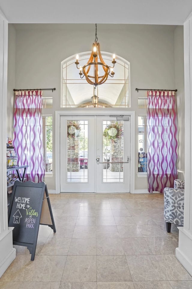 Lobby entry with double glass doors, purple curtains, and a chandelier.