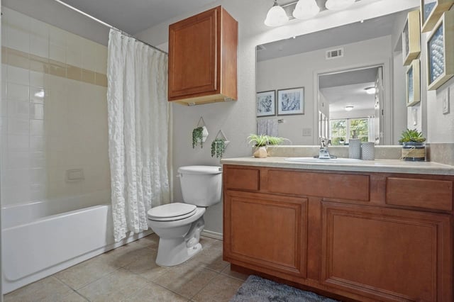 Bathroom in an apartment with tub/shower, toilet, and a wooden vanity with a mirror.