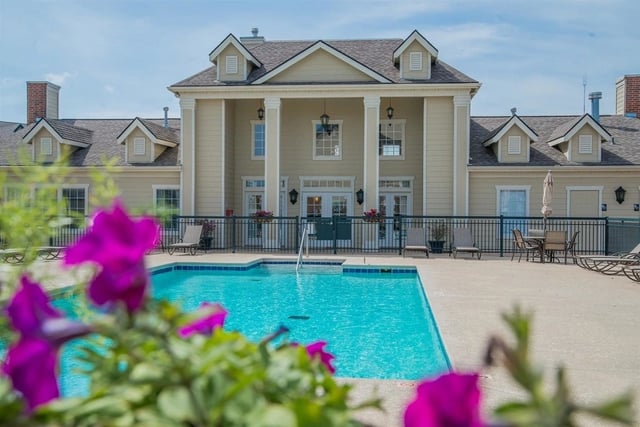 Swimming pool with lounge chairs and tables in front of a tan building with columns.