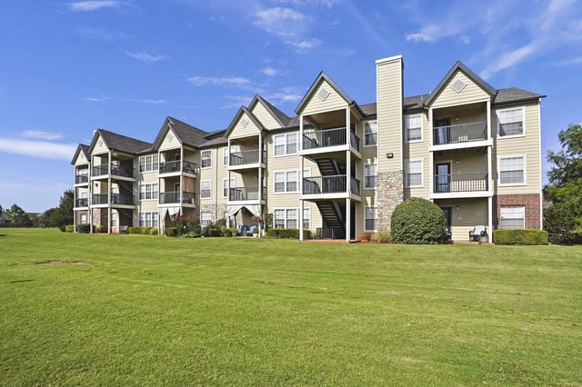 Exterior view of a beige multi-family building with balconies and a green lawn.