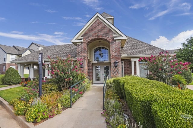 Exterior view of a brick apartment community with a landscaped walkway and colorful flowers.