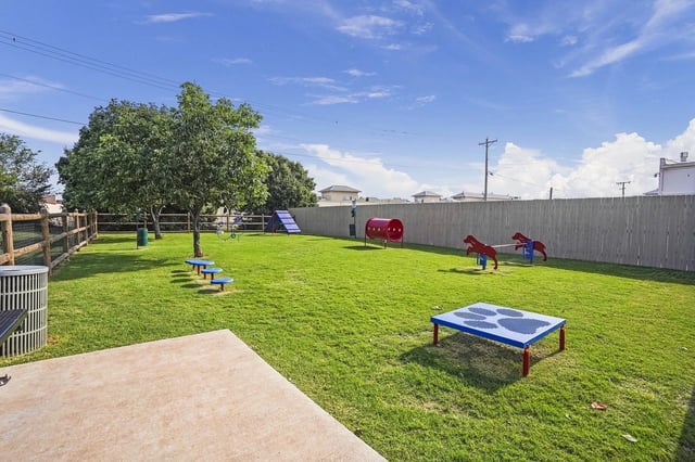 Fenced grassy community playground with a slide, seesaw, and climbing toys.