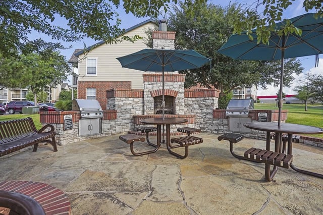 Outdoor community grilling area with stone grills, tables, benches, and umbrellas.