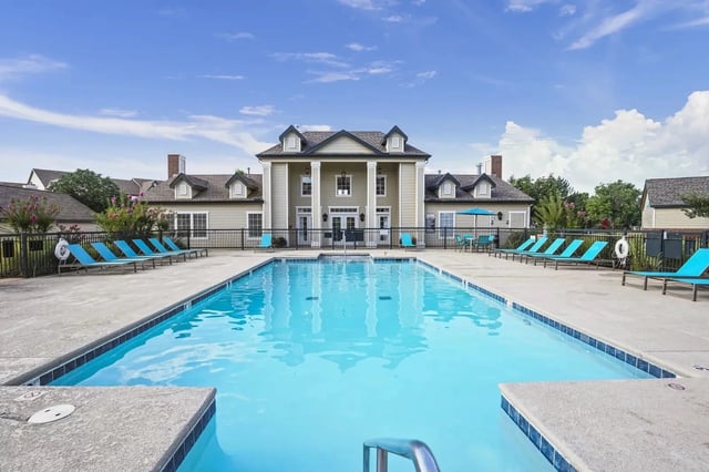 Outdoor community pool with blue lounge chairs and a clubhouse-style building in the background.