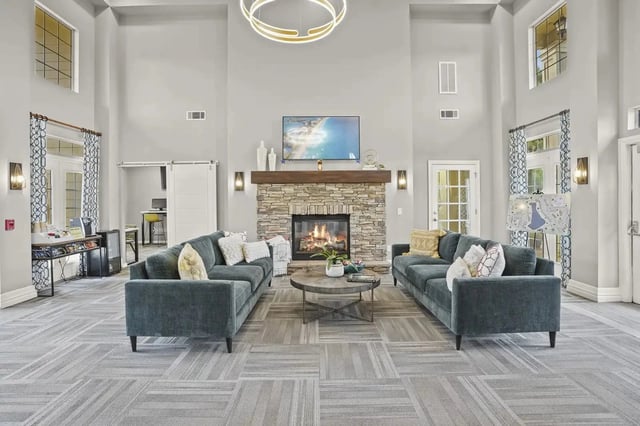 Lobby-style communal lounge with two teal sofas, a stone fireplace, and a mounted TV.