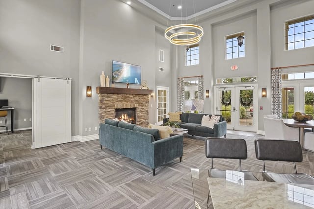 Spacious modern resident lounge with a stone fireplace, teal sofas, and large windows.