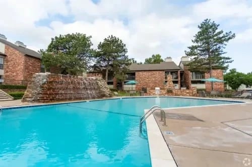 Outdoor community swimming pool with brick buildings and a stone waterfall feature.