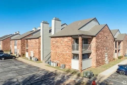 Exterior view of brick apartment buildings with balconies and a parking lot.