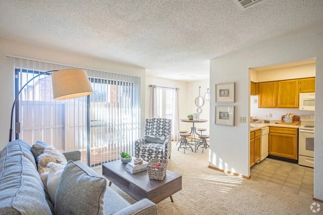 Living room with sofa, armchair, coffee table, and sliding glass doors to a balcony; kitchen visible.