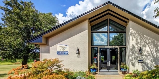 The Waters Edge leasing office entrance with large windows and doors, surrounded by landscaping.