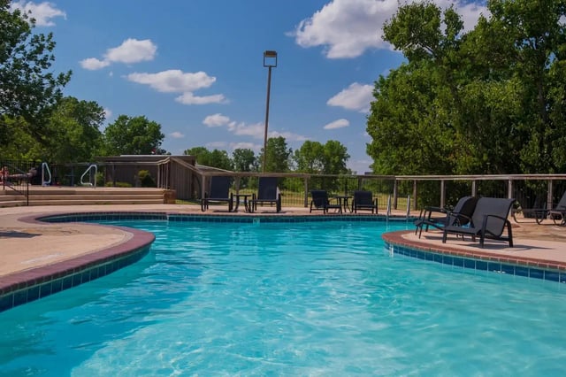 Outdoor apartment community pool with lounge chairs and surrounding trees.