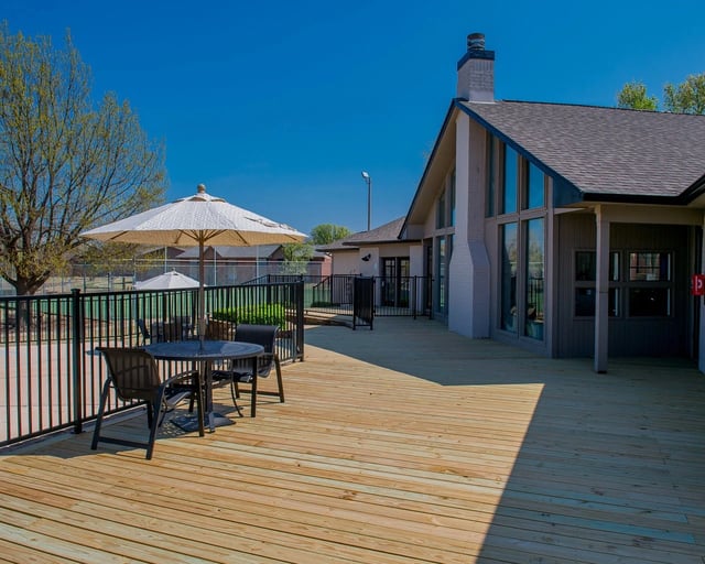 Outdoor wooden deck with table, chairs, and umbrellas beside a clubhouse.