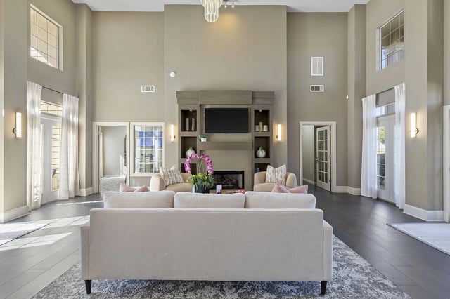 Two-story living room in a modern apartment with a neutral palette, tall windows, and a fireplace.