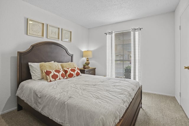Bedroom with dark wooden bed frame, nightstand, and window with blinds.