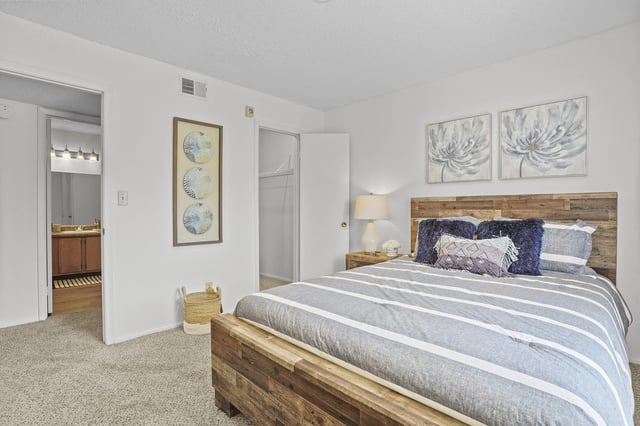 Bedroom in a modern apartment with a wooden bed, striped bedding, and wall art.