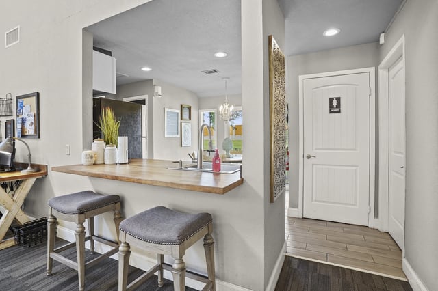 Open kitchen bar with two stools, sink, and a doorway to a restroom.