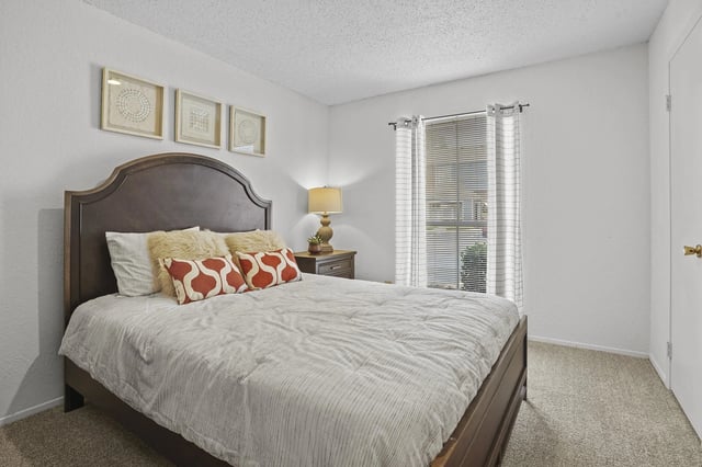 Bedroom with dark wooden bed frame, nightstand, and window with blinds.